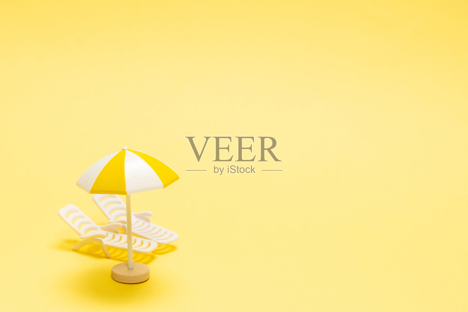 两张日光躺椅和一把黄色背景的红伞。照片摄影图片