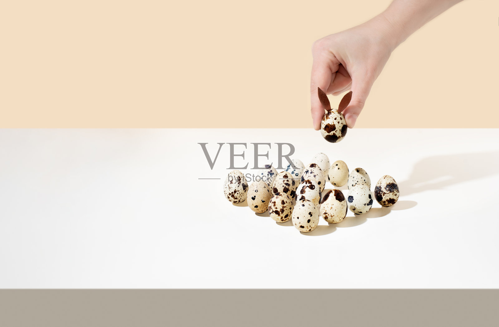 女性手把鹌鹑蛋与其他蛋排成一排，形成复活节兔子的形状，现代等距概念。照片摄影图片