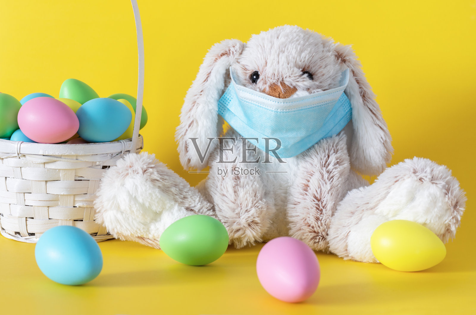 复活节兔子在面具和彩色蛋篮子在黄色的背景。假日期间冠状病毒概念。照片摄影图片