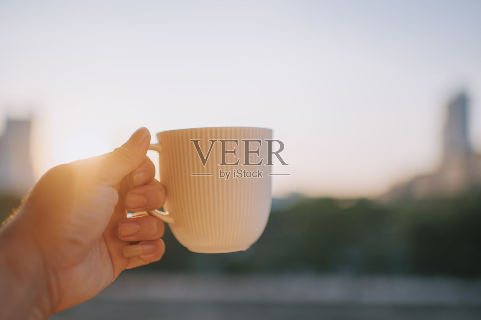 人的手拿着咖啡杯，背景是日出照片摄影图片