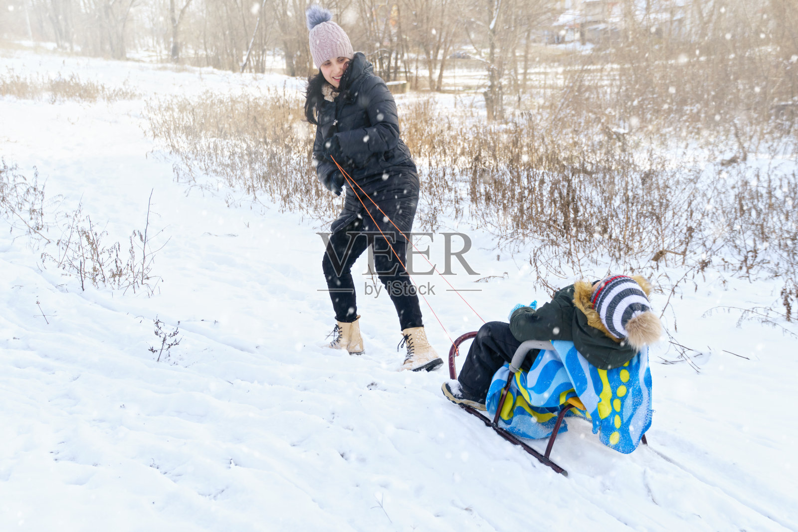 家庭游戏和雪橇在冬天户外，母亲和孩子们在下雪的冬天有乐趣照片摄影图片