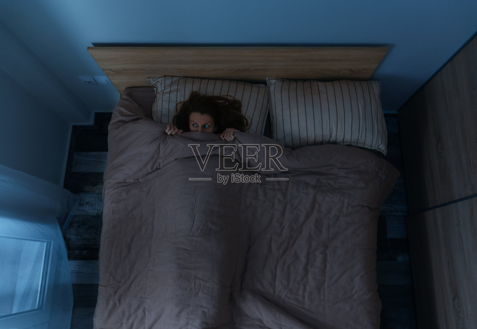 害怕的女人晚上独自躺在床上。照片摄影图片