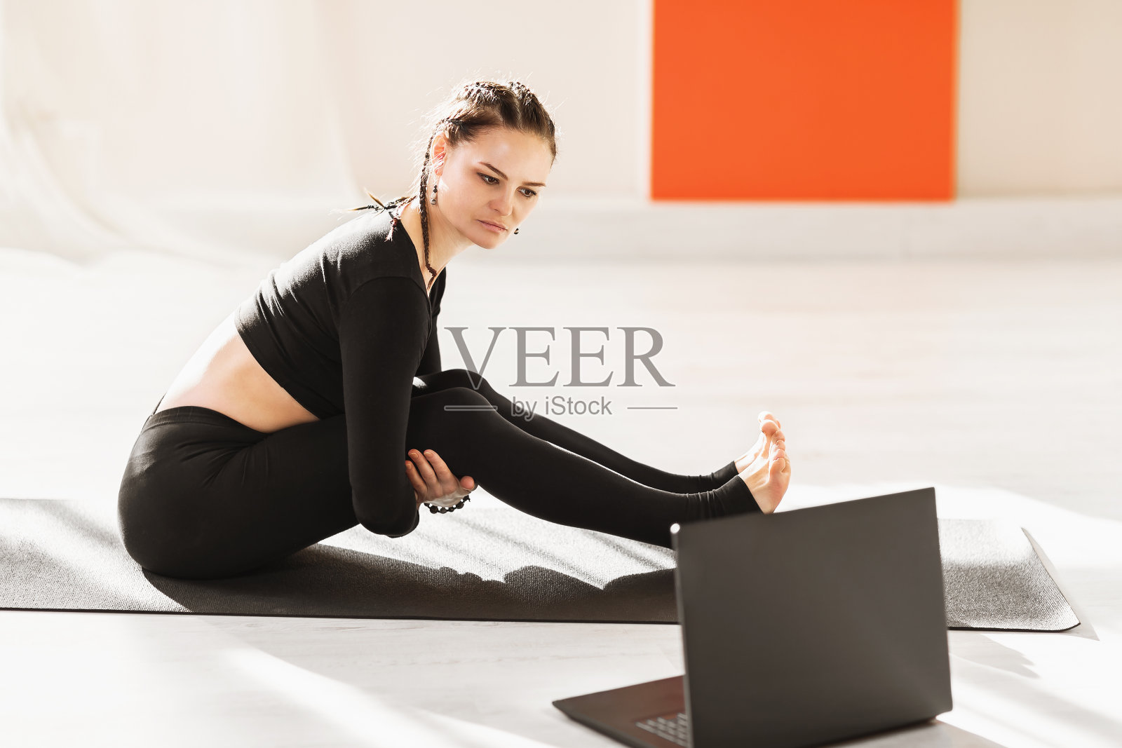 一位穿着黑色运动服的女士正坐在体操垫上，仔细看着笔记本电脑的屏幕。在线体育概念照片摄影图片