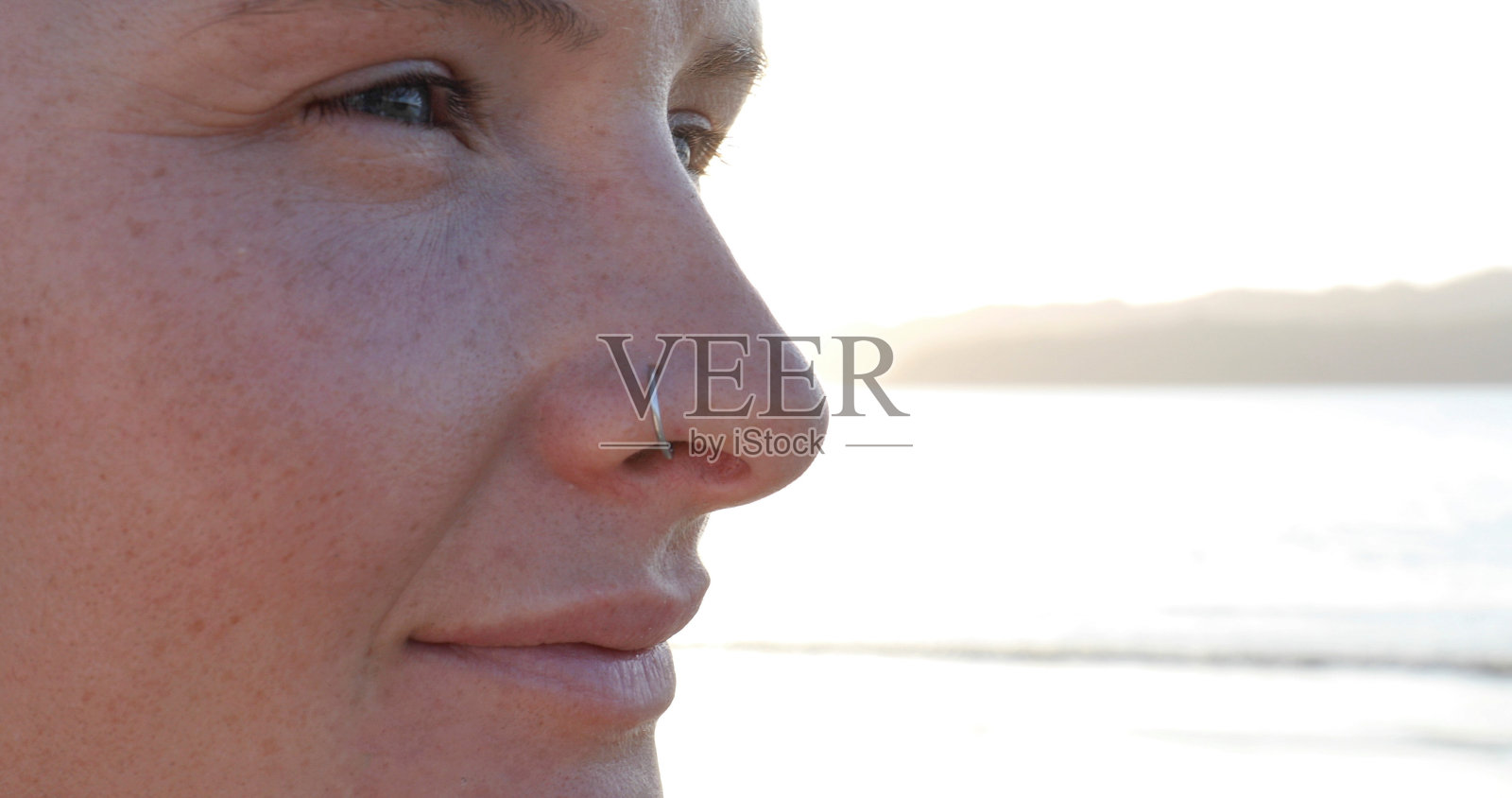 近距离观察年轻女子的脸，因为她在日出时在海滩上休息照片摄影图片