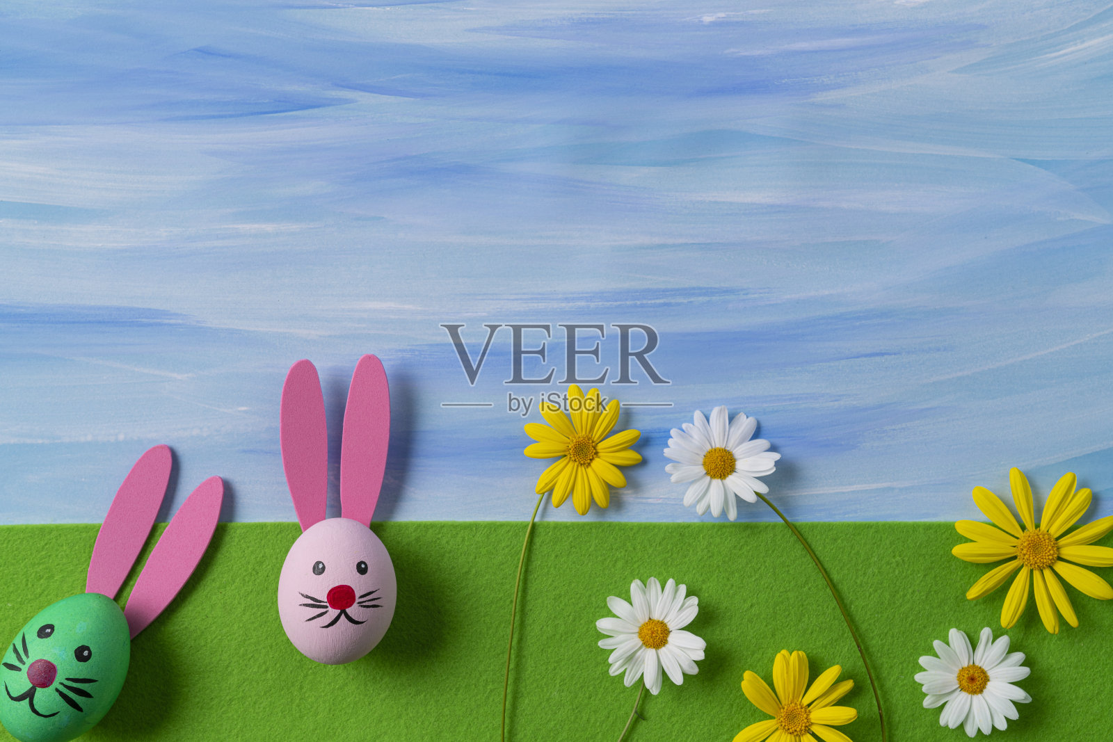 在绿色的毛毡上画有复活节兔子的脸和水彩蓝色的天空照片摄影图片