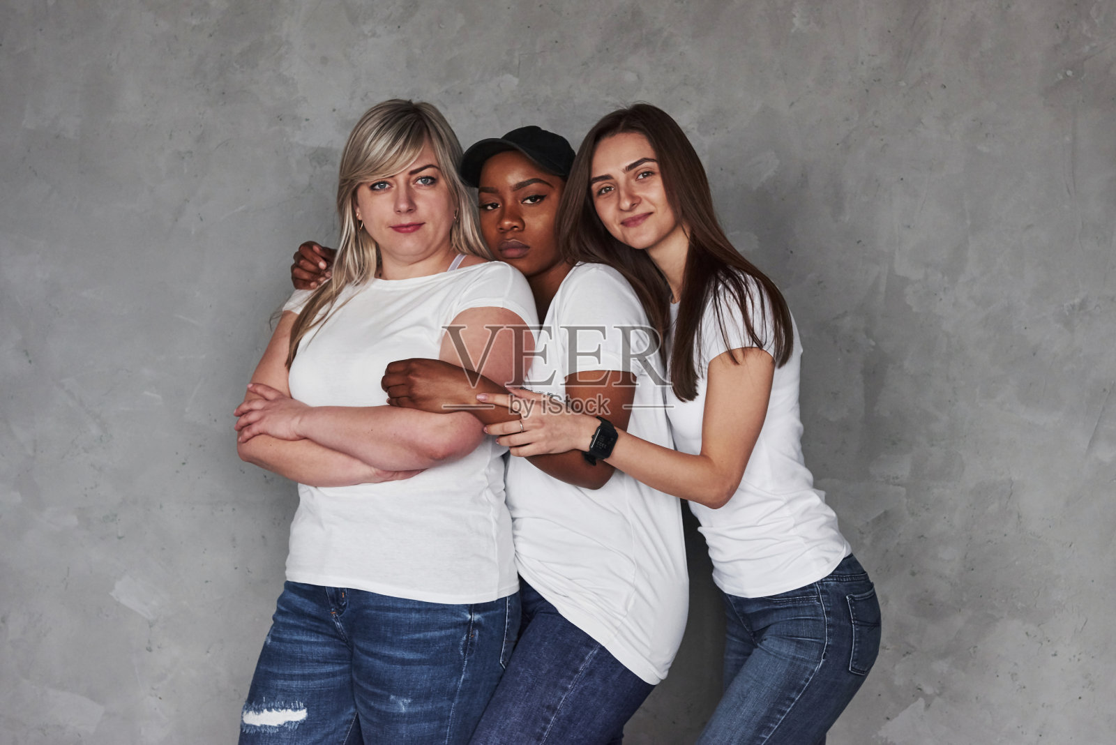 在同样的衣服。在灰色背景下，一群多民族妇女站在演播室里照片摄影图片