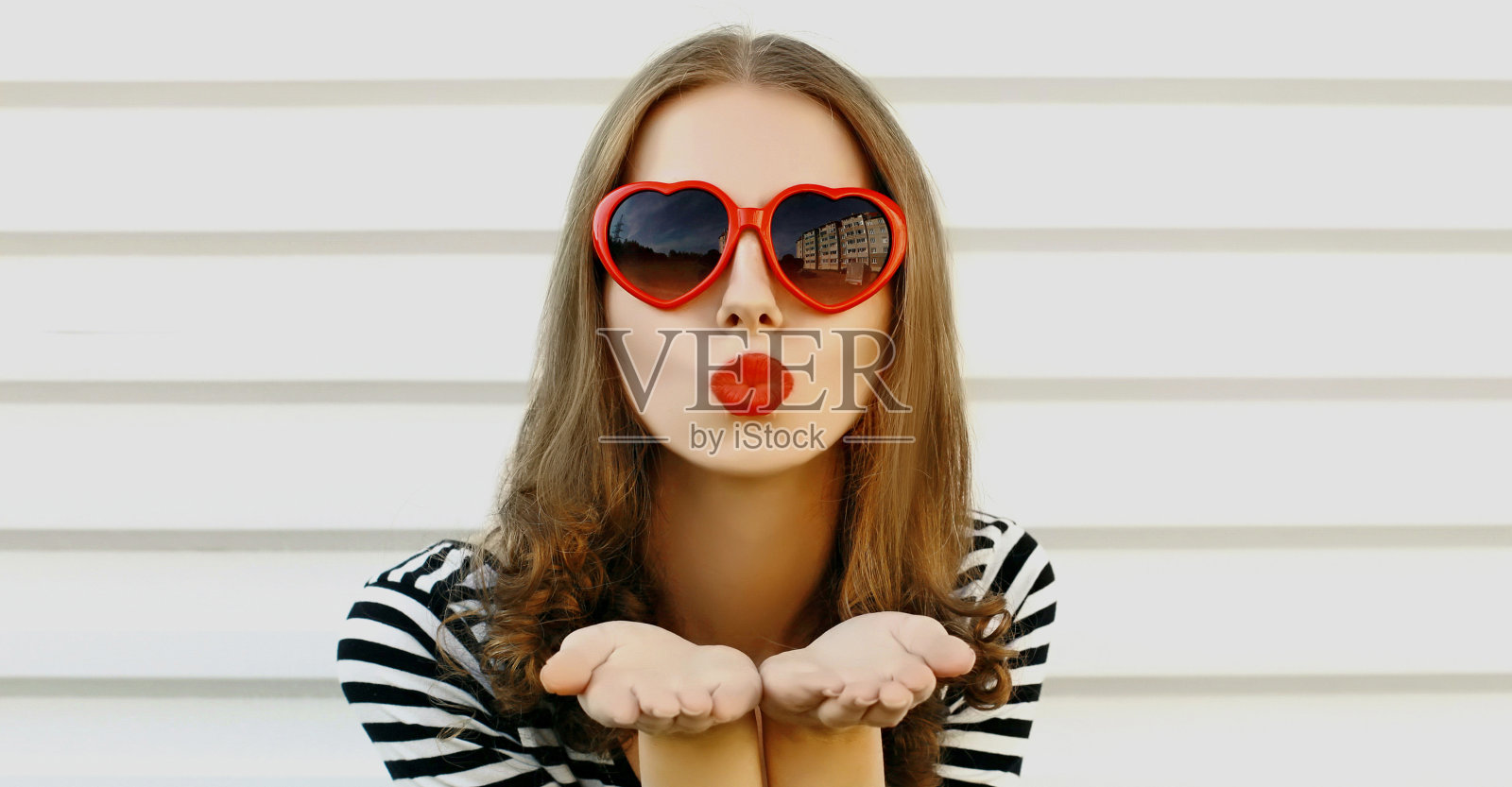 美丽的年轻女子的肖像吹她的红色嘴唇发送甜蜜的空气吻在白色的背景照片摄影图片