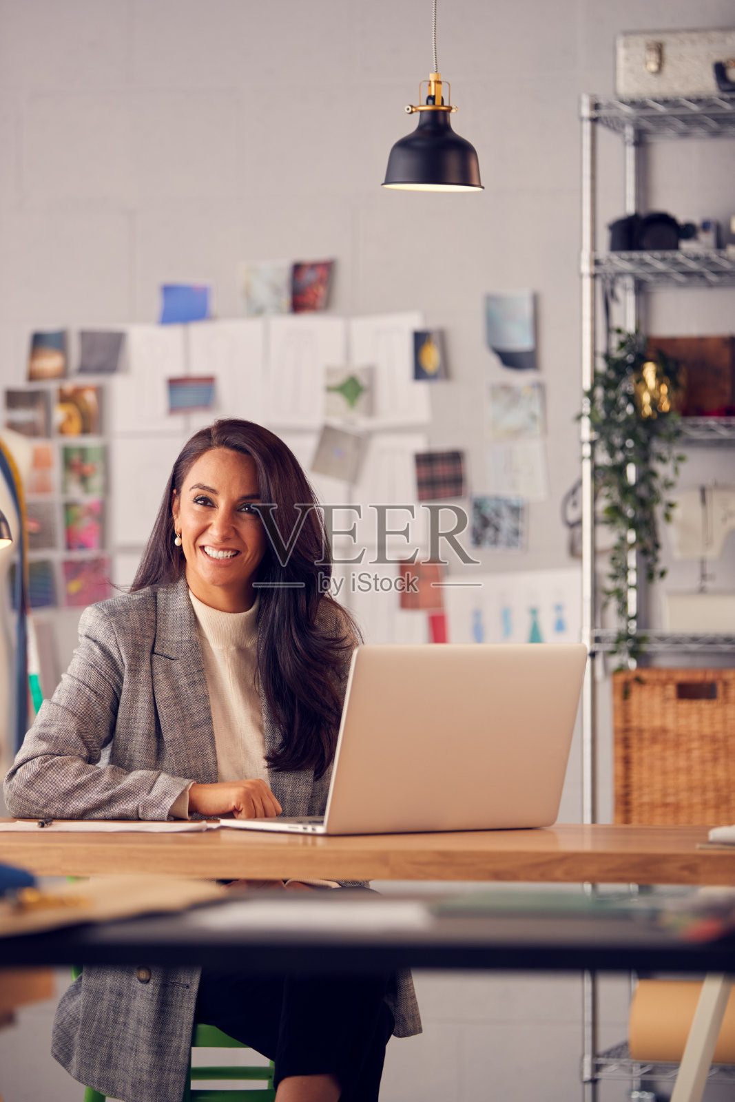 女时装设计师在工作室坐在书桌上用笔记本电脑工作的肖像照片摄影图片