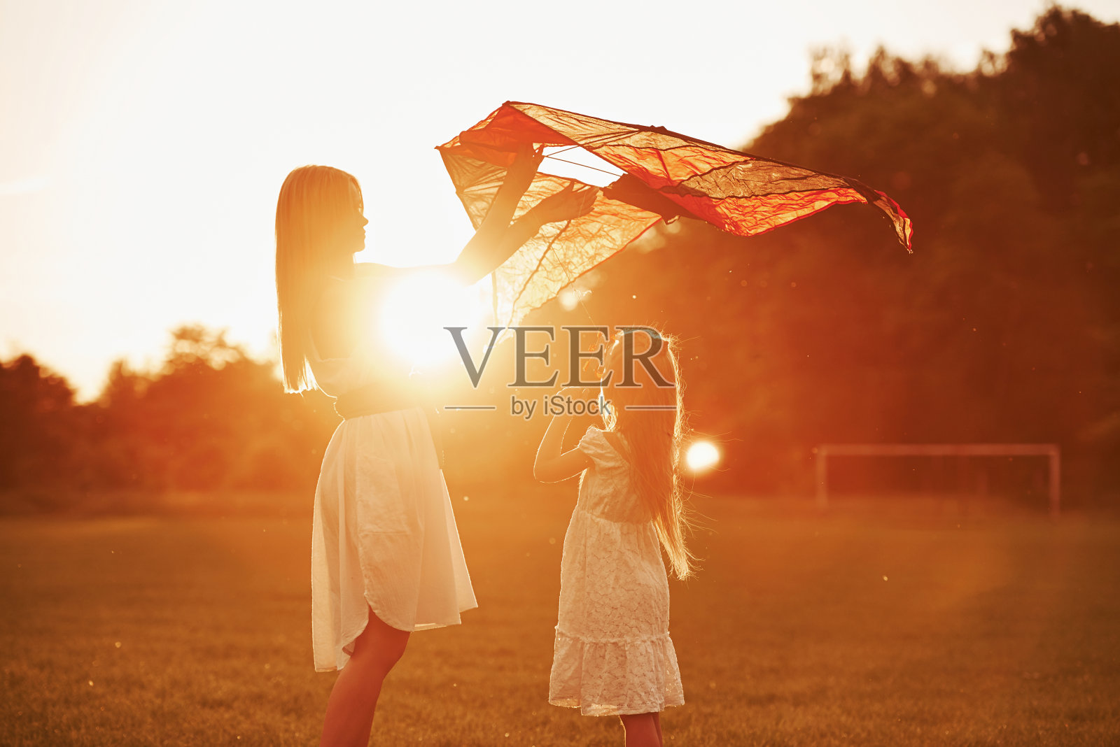 橙色的日落。妈妈和女儿在田野里玩风筝。美丽的大自然照片摄影图片