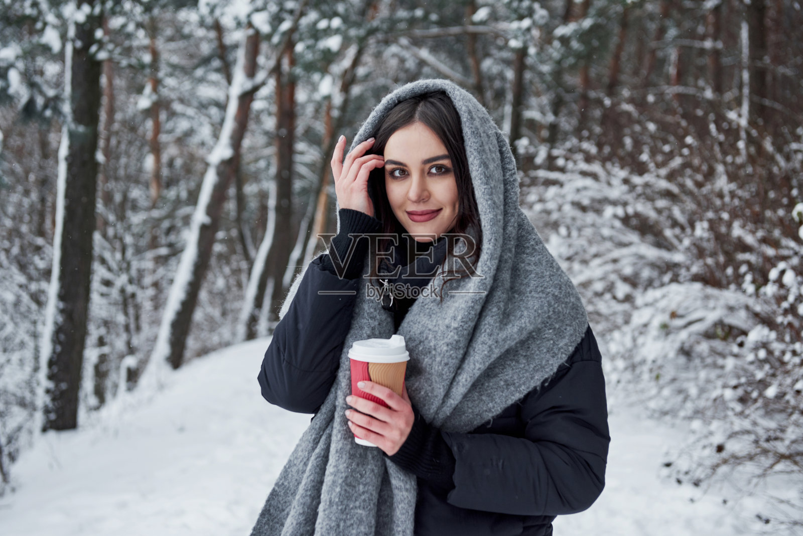 一个快乐的女人摸着她美丽的头发。女孩穿着暖和的衣服喝着咖啡在冬天的森林里散步照片摄影图片