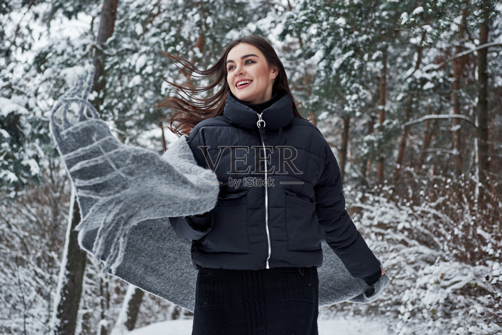 运动的照片。冬季森林里穿着黑色夹克和灰色围巾的迷人女人的肖像照片摄影图片