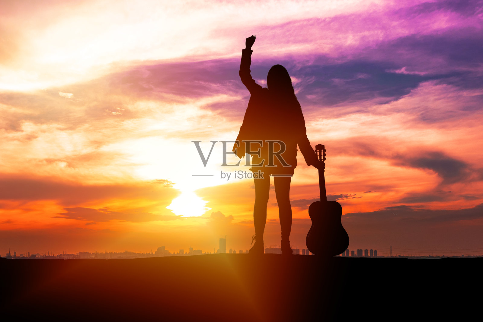 剪影旅行者年轻女性音乐家拿着吉他和她的手，而站在日落背景与拷贝空间。美丽的天空日出与年轻女孩感觉自由与原声吉他。照片摄影图片