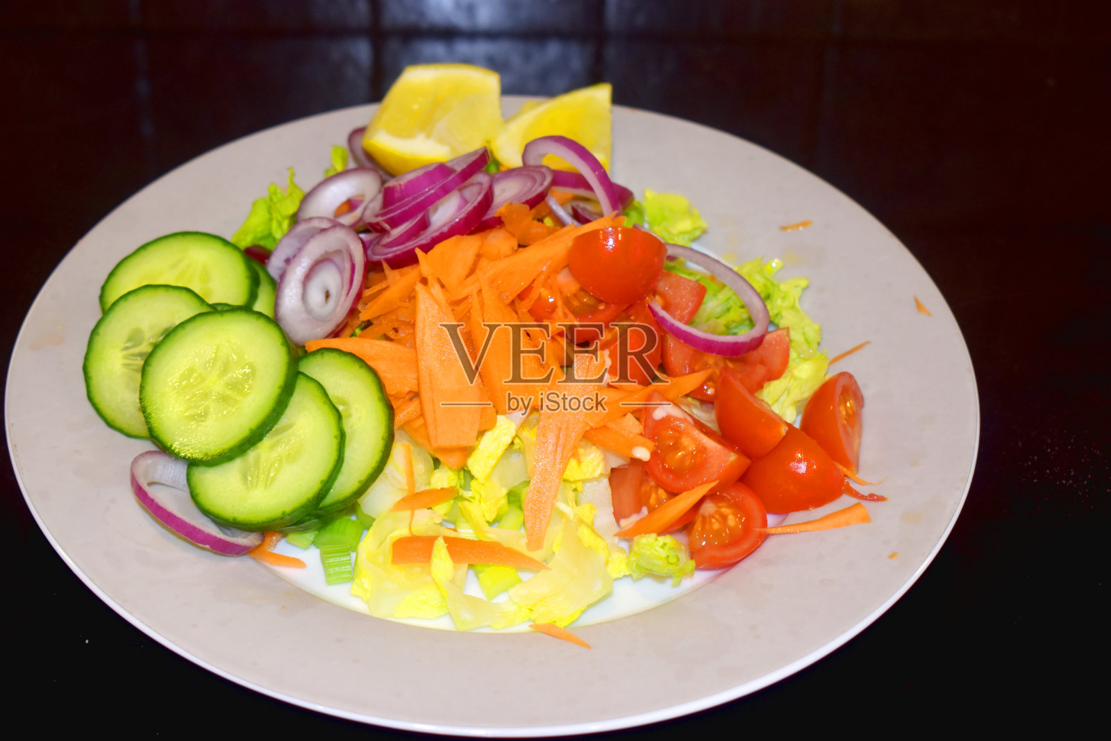 将黄瓜、胡萝卜、番茄、红洋葱和绿生菜切成片，放在有背景的灰色盘子上，做成沙拉用的有机蔬菜。健康的食物和简单的在家烹饪。照片摄影图片