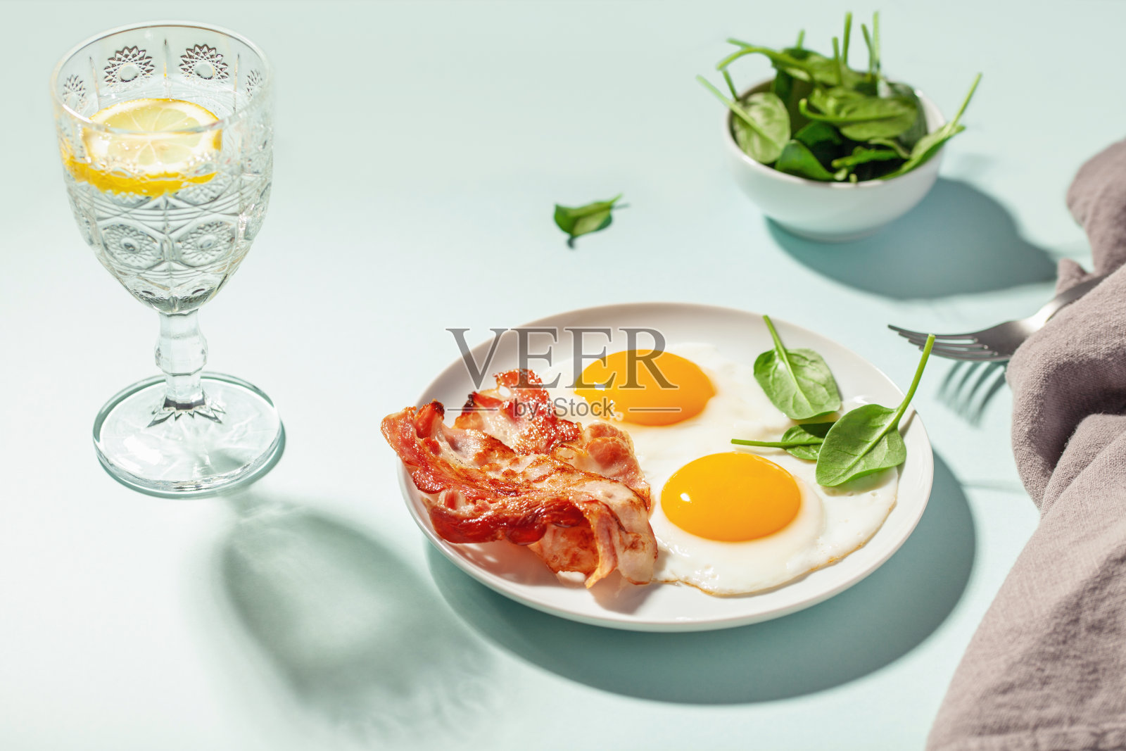 英式早餐——鸡蛋、培根和菠菜叶装在一个盘子里。和柠檬水。硬光。照片摄影图片