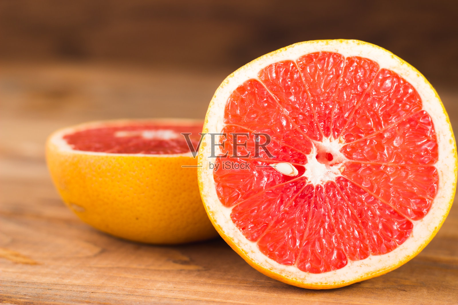 两半葡萄柚放在木板上。木制背景上的红色柑橘照片摄影图片