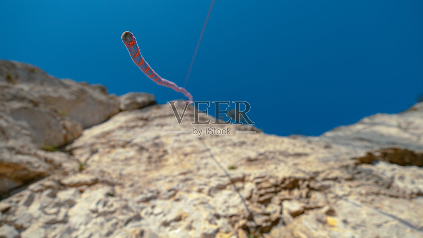 从下往上，DOF:蓝色和红色的绳索悬挂在高耸的悬崖顶部。照片摄影图片