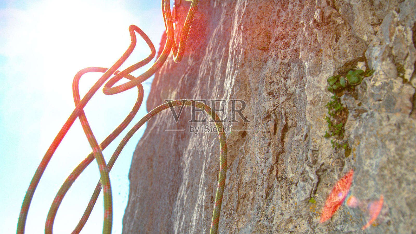 近镜头，镜头光晕:绿色和红色的绳索从高耸的悬崖顶端落下。照片摄影图片