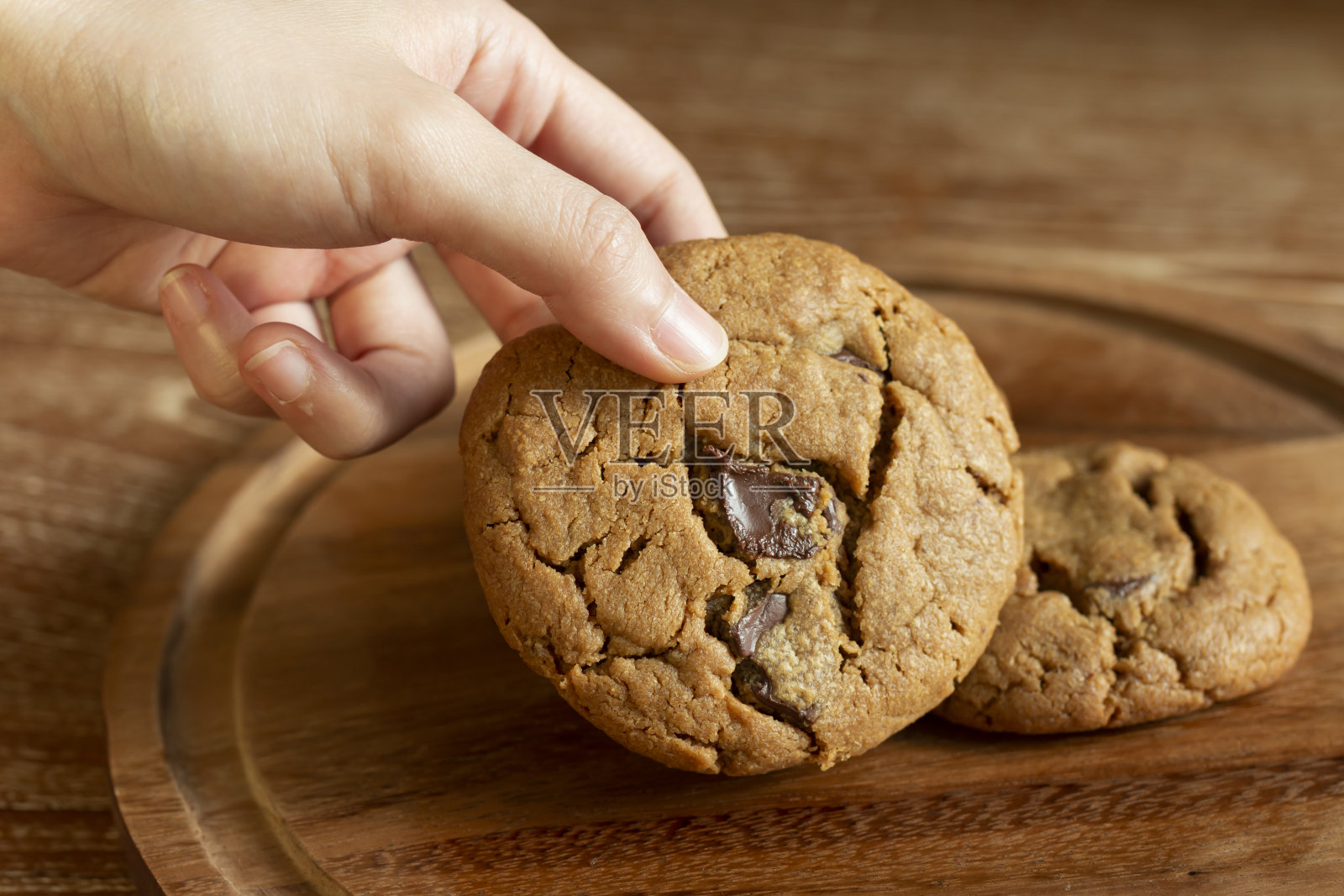 美味的巧克力饼干放在木桌上的木盘上。新鲜烘焙的巧克力饼干放在质朴的木桌上。照片摄影图片