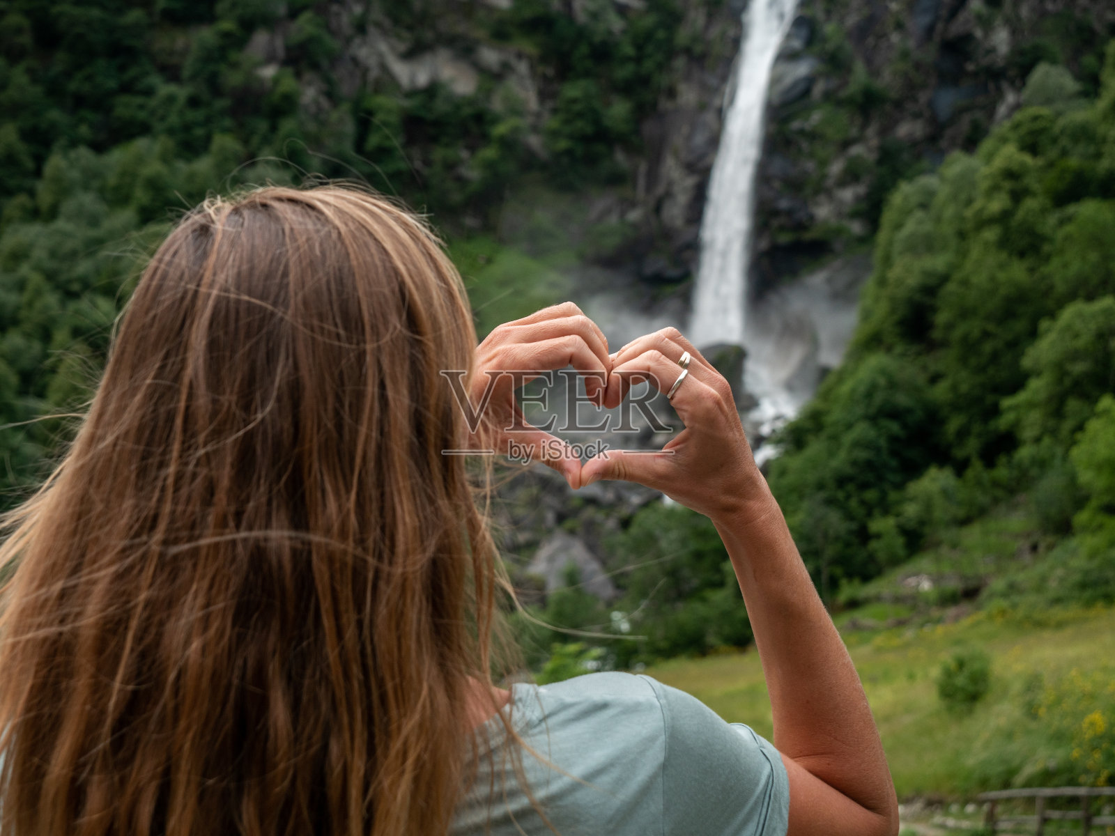 女人热爱自然，她用双手在瀑布上做了一颗心照片摄影图片