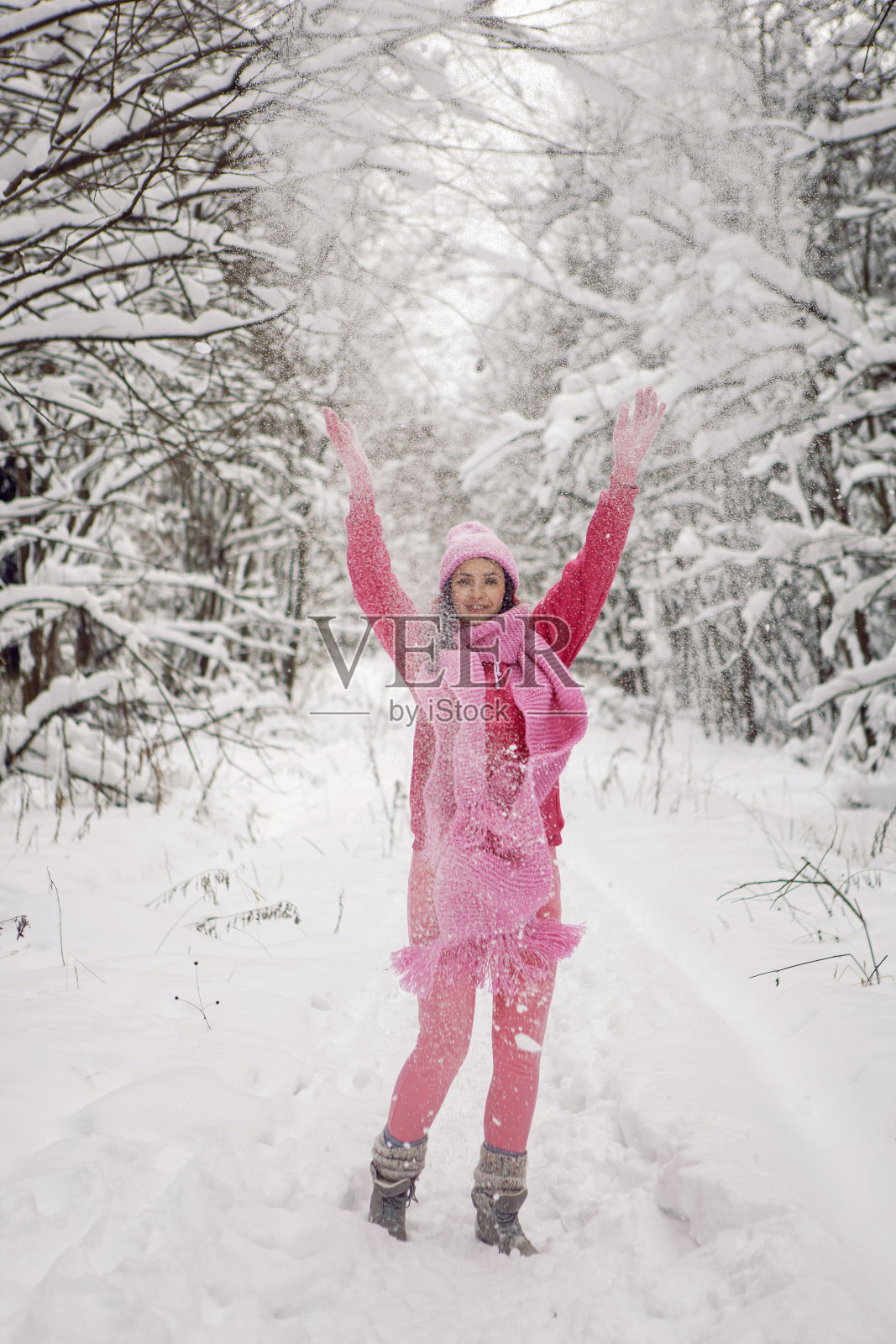 一个穿着粉红色衣服，夹克，针织围巾和帽子的女人站在雪地里的森林里照片摄影图片