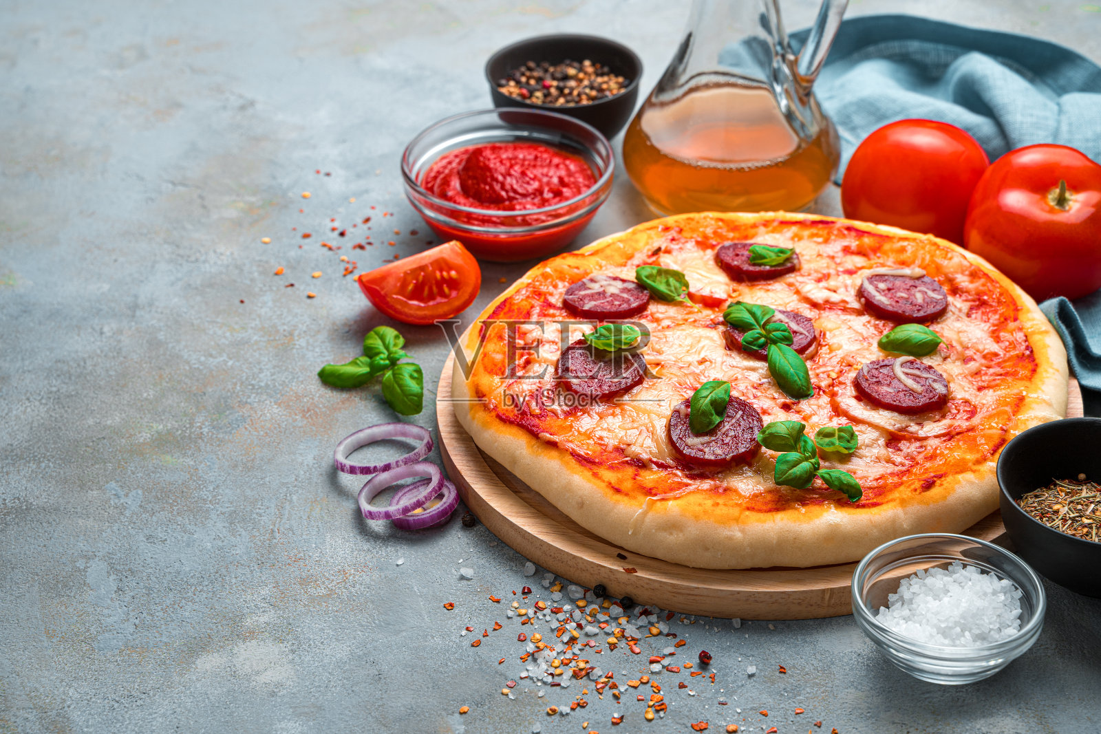 在混凝土灰色背景下，美味的披萨上有意大利腊肠和配料照片摄影图片
