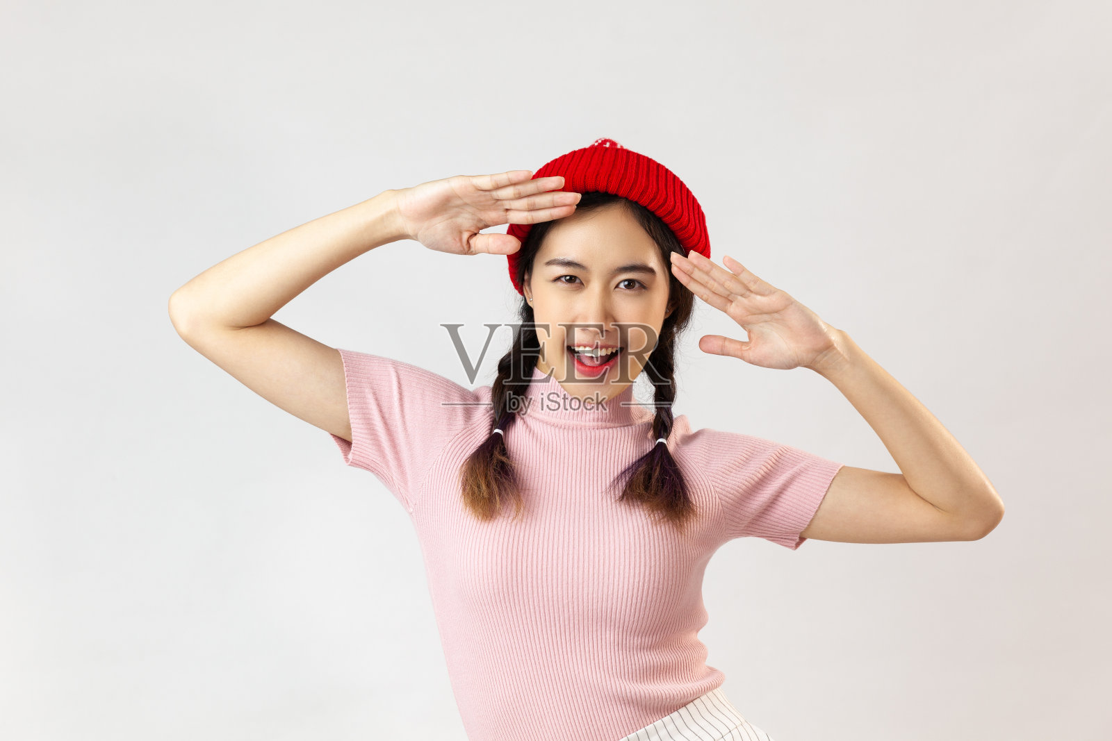 年轻女子梳着辫子，穿着粉红色的高领衬衫和红帽子在白色的背景上摆姿势照片摄影图片