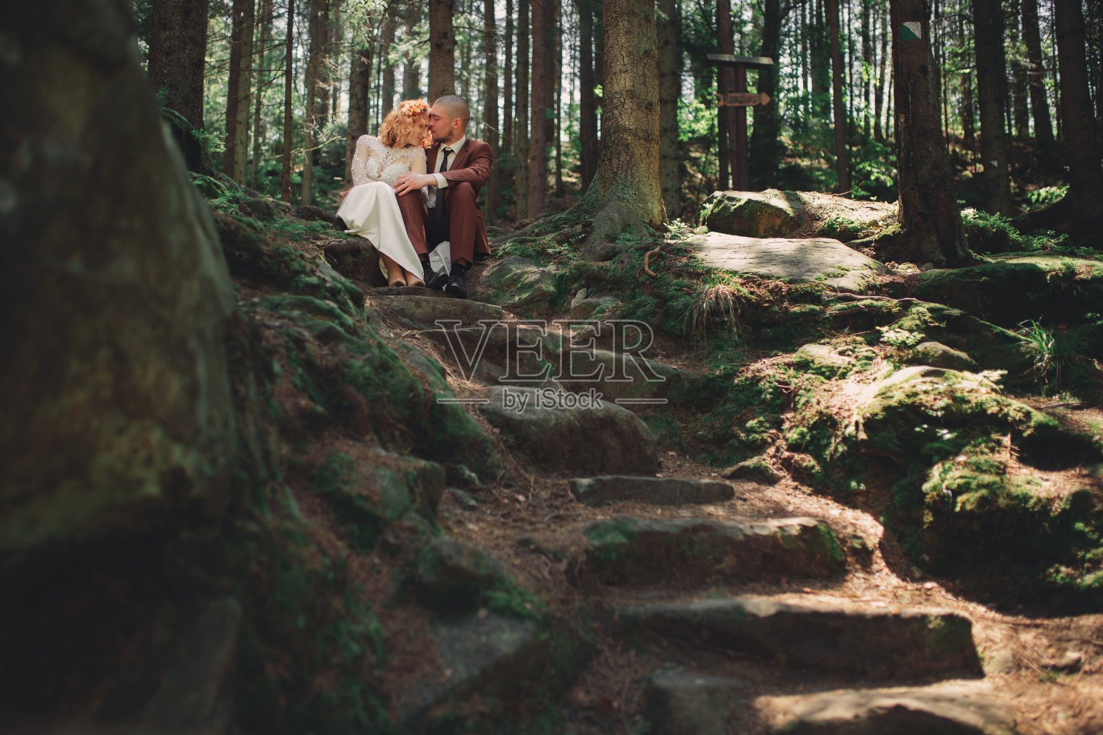 快乐时尚的新婚夫妇在夏日的绿色森林里。穿着白色长裙的新娘和穿着红色套装的新郎拥抱在一起。结婚的那一天。照片摄影图片