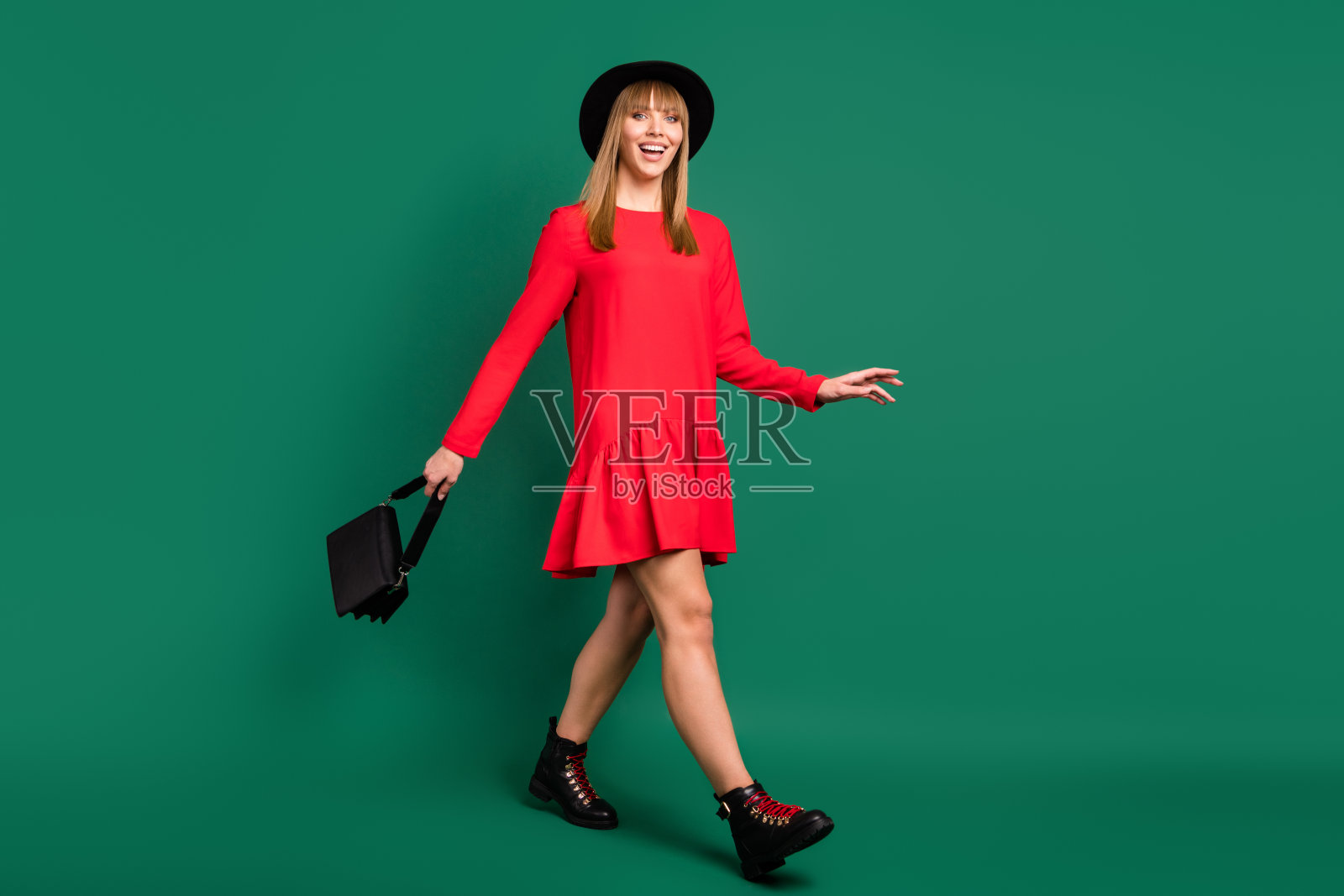 快乐女士的照片，享受散步，拿着钱包，戴着帽子，红色的衣服，鞋子孤立的绿色背景照片摄影图片