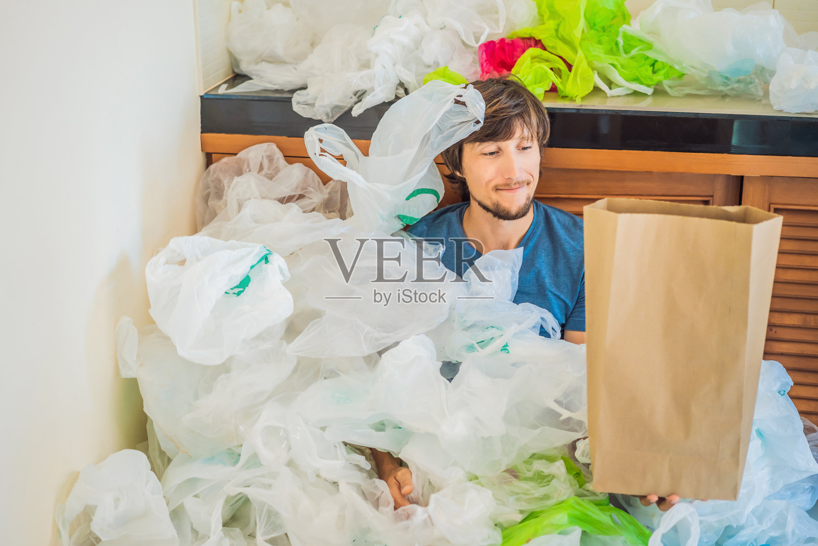 在一堆塑料袋中拿着纸袋的男人。“零浪费”的概念。世界环境日的概念照片摄影图片