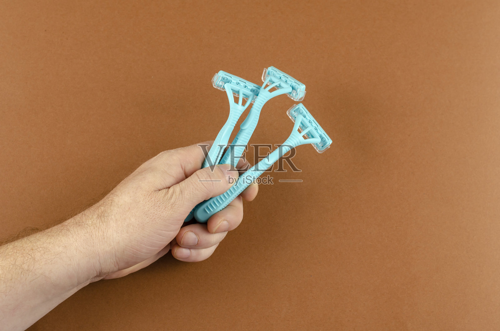 手持浅蓝色塑料剃须刀，背景为棕色。照片摄影图片