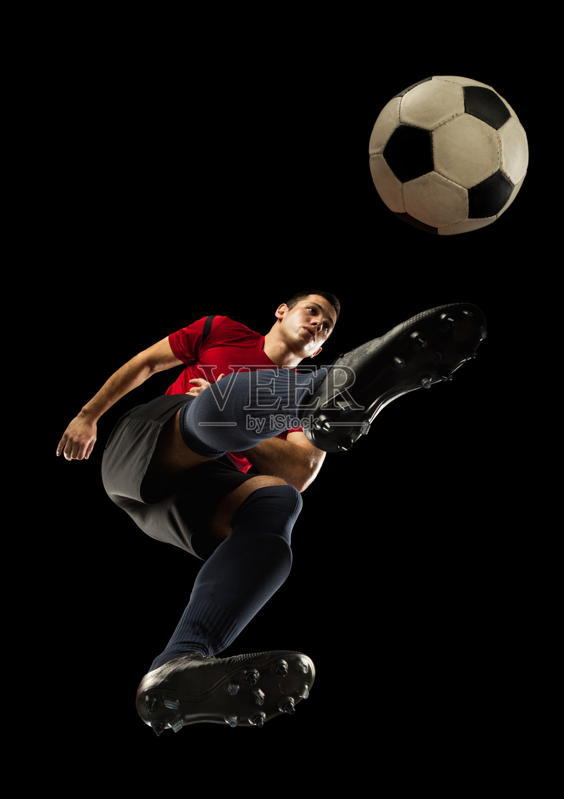 年轻的白人足球，足球运动员在行动，运动孤立在黑色背景，从底部看。运动、运动、能量和动态的概念。照片摄影图片