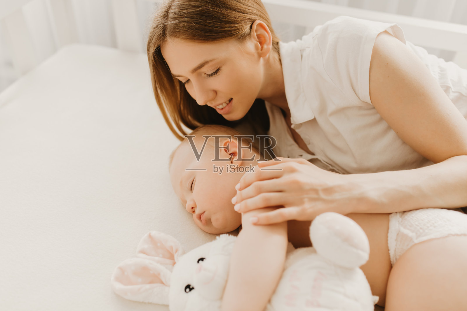 美丽的年轻母亲亲吻在床上熟睡的新生儿照片摄影图片