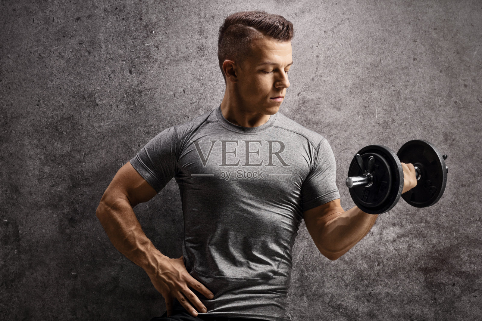 健美运动员拄着哑铃在生锈的墙上锻炼照片摄影图片