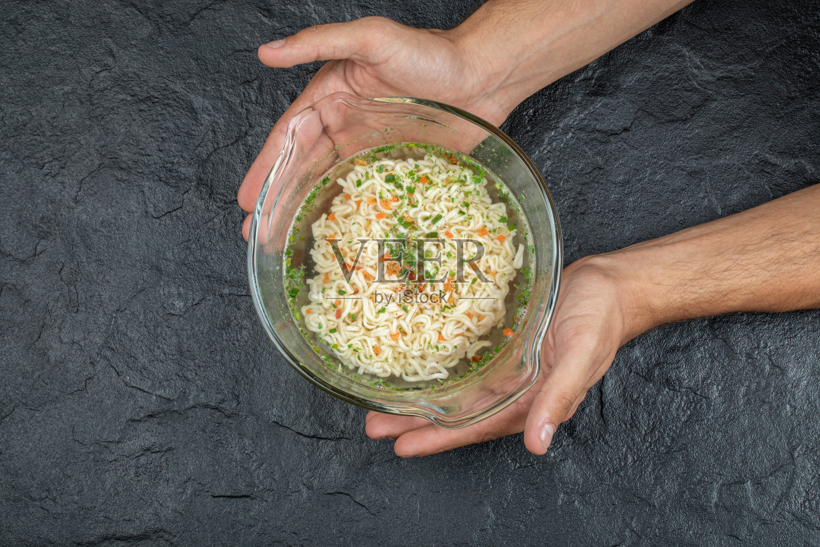 在黑暗的背景下，手里拿着一个玻璃盘子，上面放着美味的面条照片摄影图片