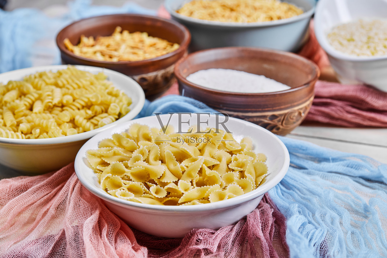 各种生面食和面粉碗摆放在木桌上，上面铺着蓝色和粉红色的桌布照片摄影图片