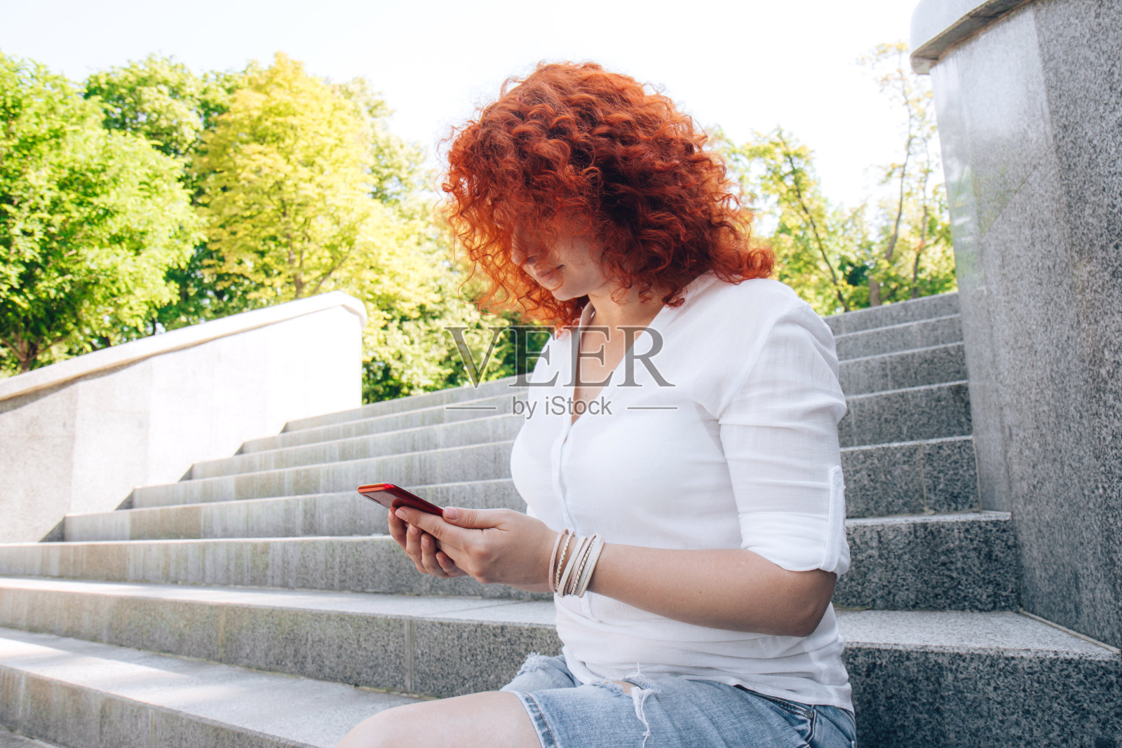 一名长着红色卷发的妇女在街上看她的手机照片摄影图片