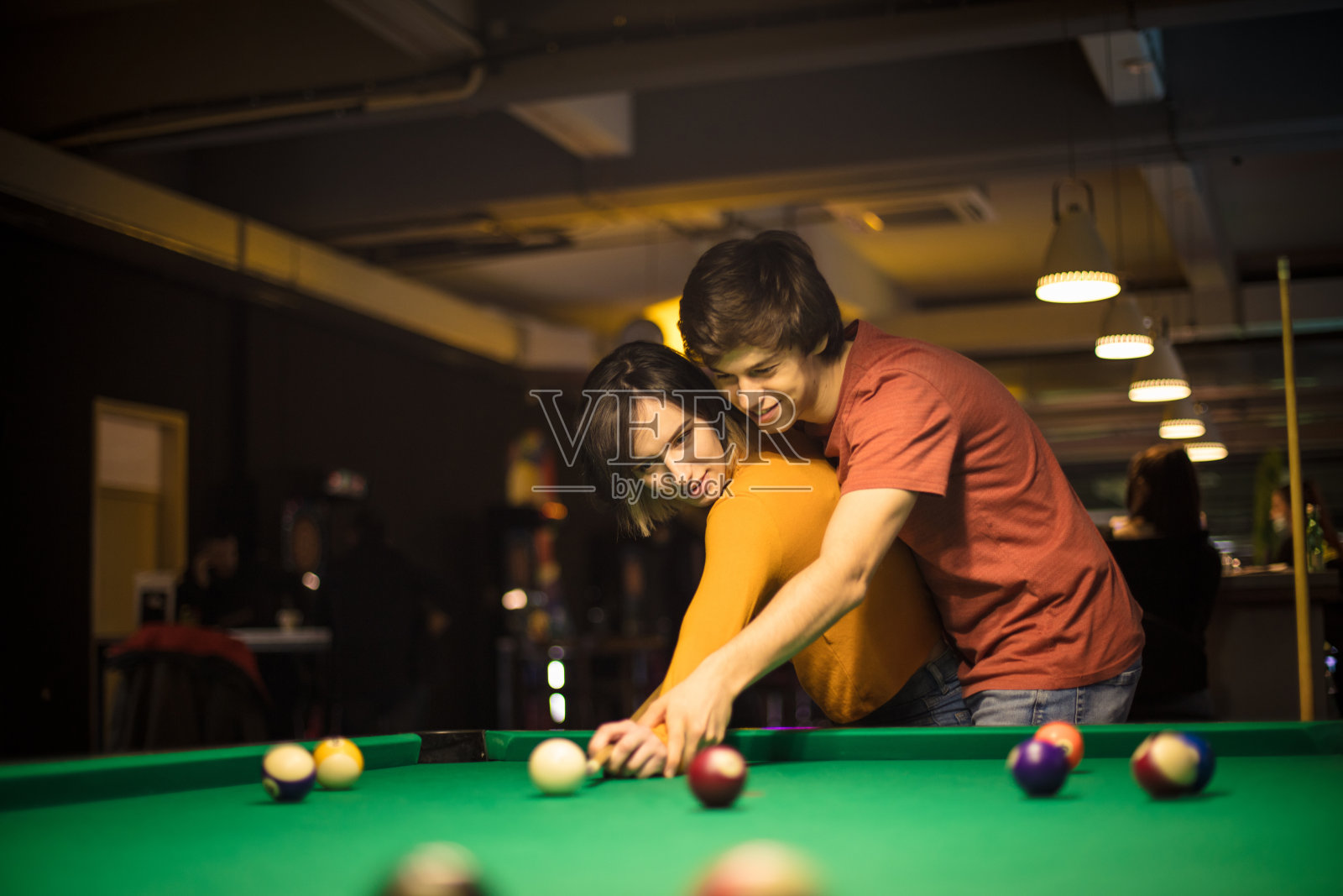 年轻夫妇花时间在台球室。男友教女友打台球。照片摄影图片