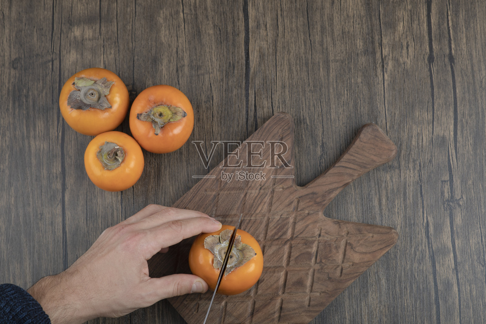 男把柿子在木板上切成两段照片摄影图片