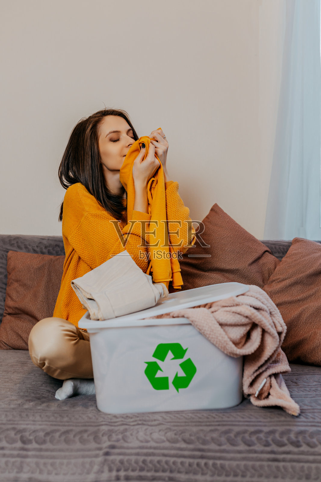 一名妇女把旧衣服分类放入有回收标志的白色容器中。白色容器上的绿色回收标志。扔掉旧衣服的女人。照片摄影图片