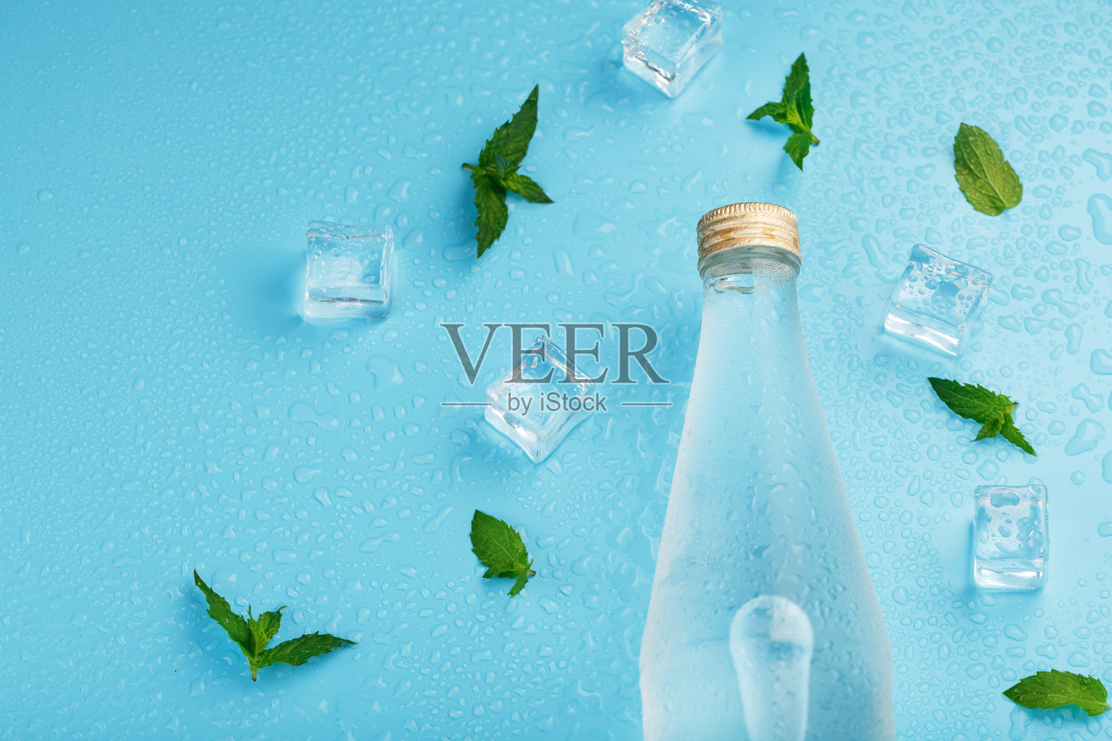 一瓶冰饮料，冰块，水滴和薄荷叶在蓝色的背景。照片摄影图片