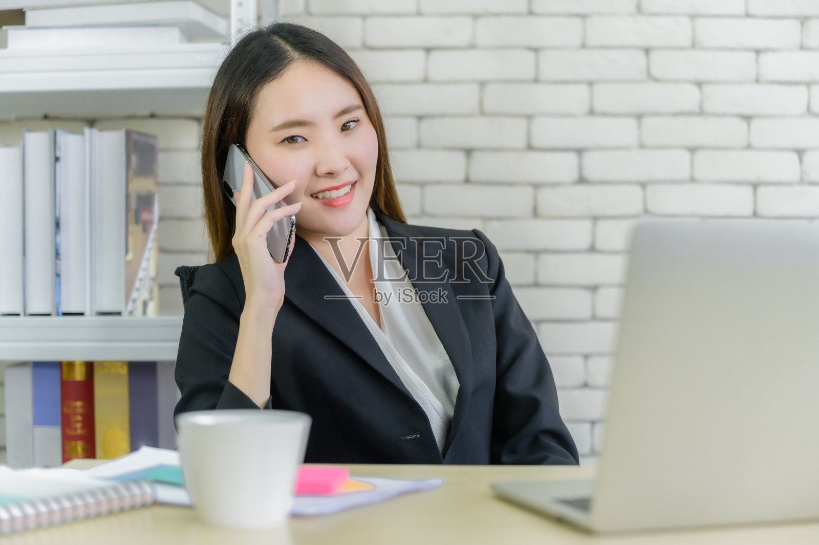 亚洲商务女性的肖像西装微笑坐在椅子上，通过智能手机交谈照片摄影图片