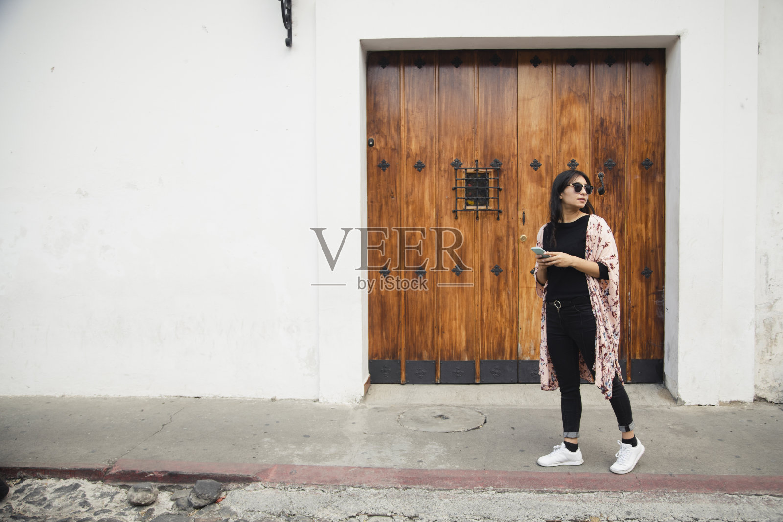 一名西班牙裔妇女带着手机走在殖民城市的全貌，一名游客在危地马拉安提瓜边走边发短信照片摄影图片