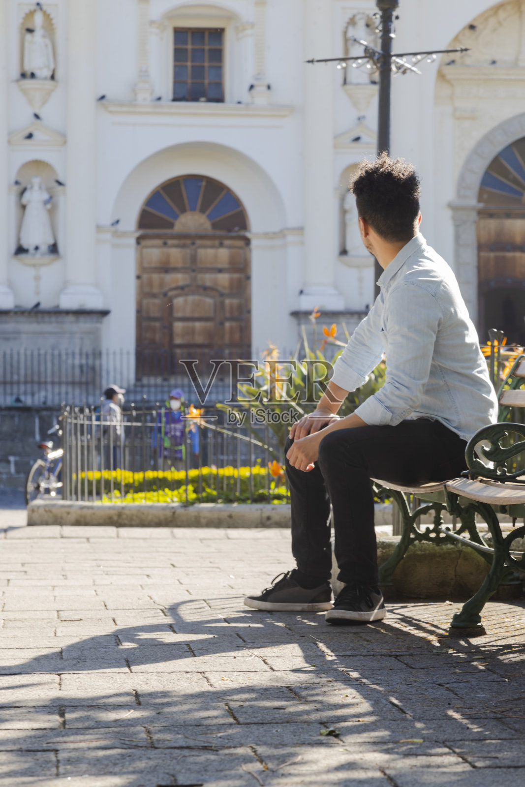 西班牙裔年轻人坐在危地马拉安提瓜和巴布亚的圣何塞大教堂前——年轻的游客看着鸽子飞过殖民城市——危地马拉安提瓜和巴布亚中央公园的教堂照片摄影图片