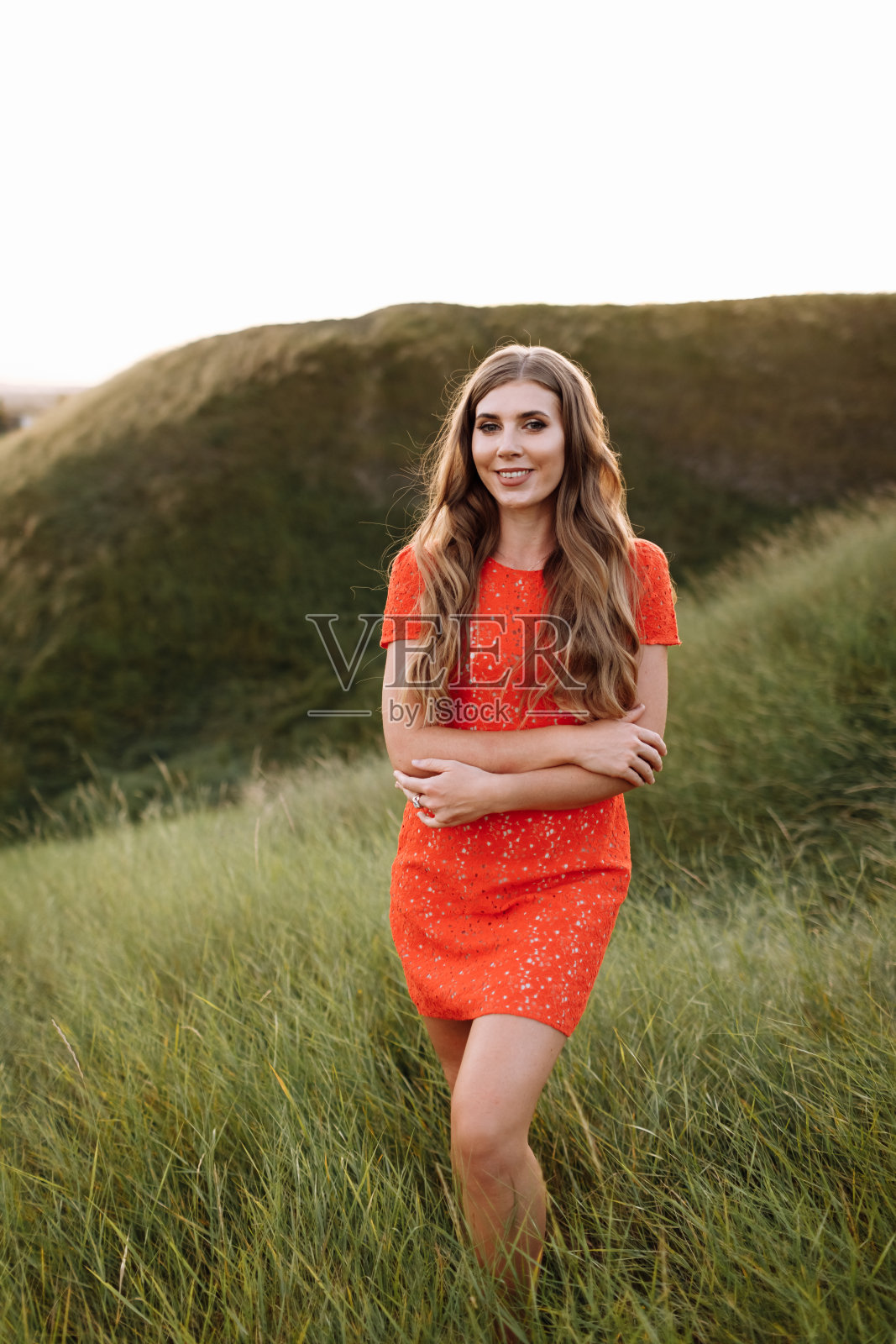 一个穿着红衣服的美丽女子的肖像在草地上的田野，自然在暑假。日落时分，在公园里有一头长长的卷发的女孩。照片摄影图片