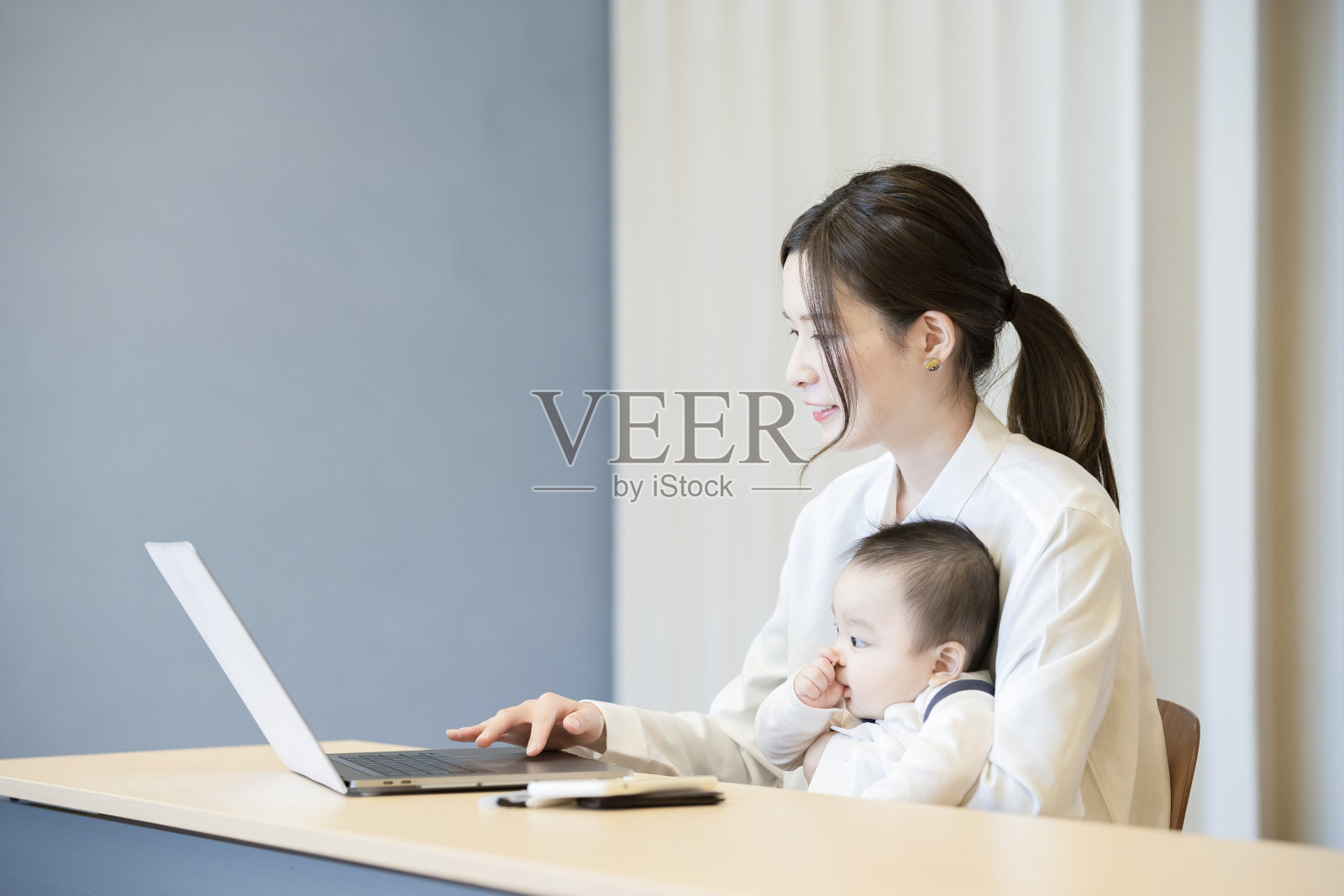 抱着婴儿操作笔记本电脑的女人照片摄影图片