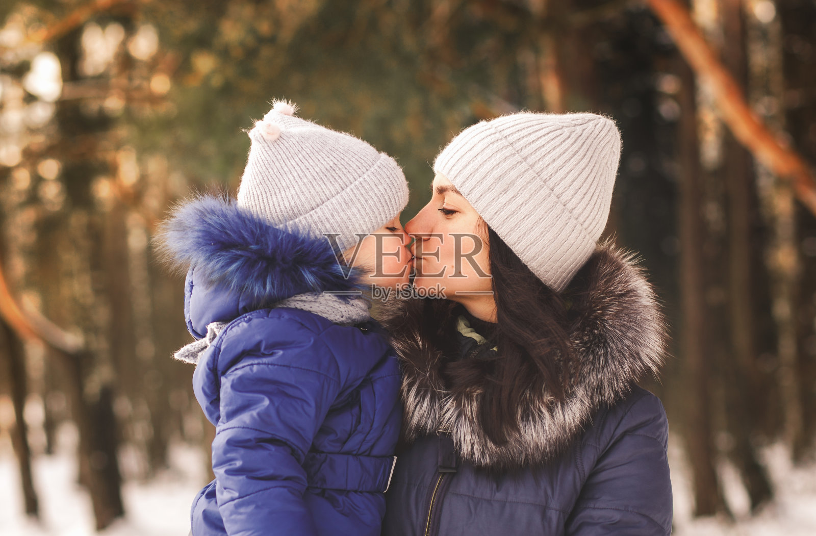 冬天，妈妈在树林里散步时亲吻了一个小女孩。母爱照片摄影图片