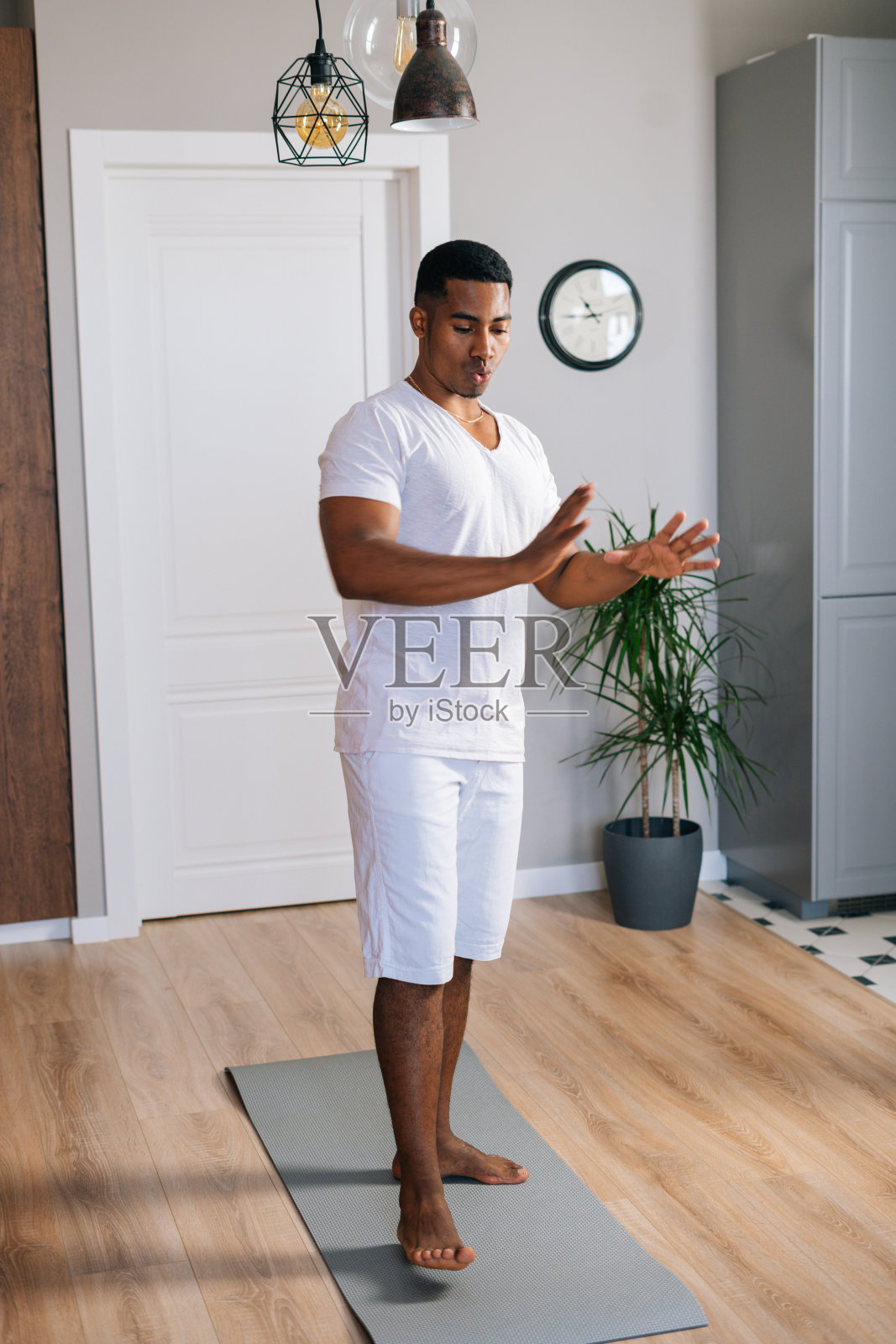 运动的非洲裔美国年轻人在明亮的家庭房间里站在瑜伽垫上热身。照片摄影图片