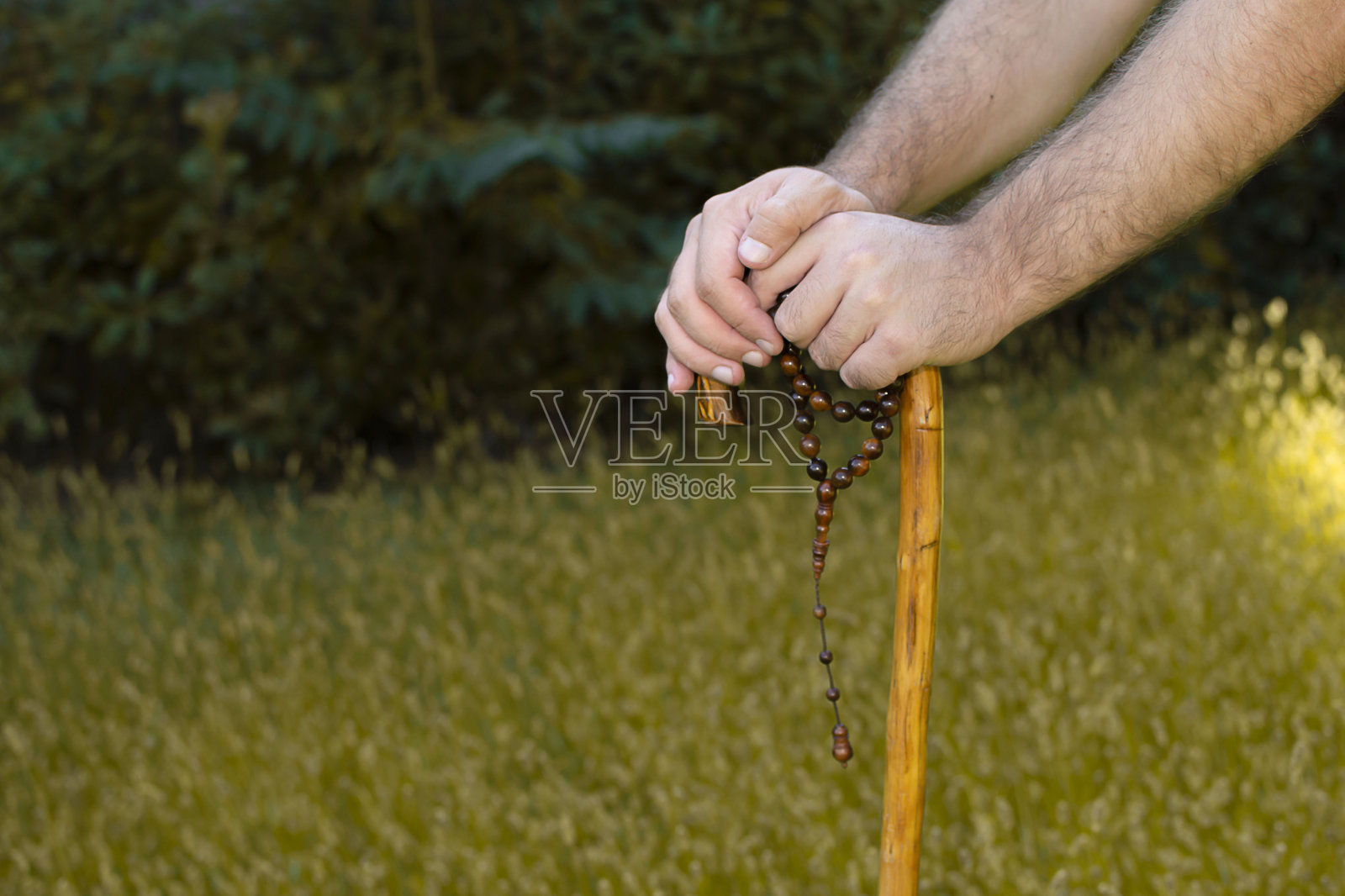 年长的穆斯林老人户外祈祷，手持拐杖和念珠照片摄影图片