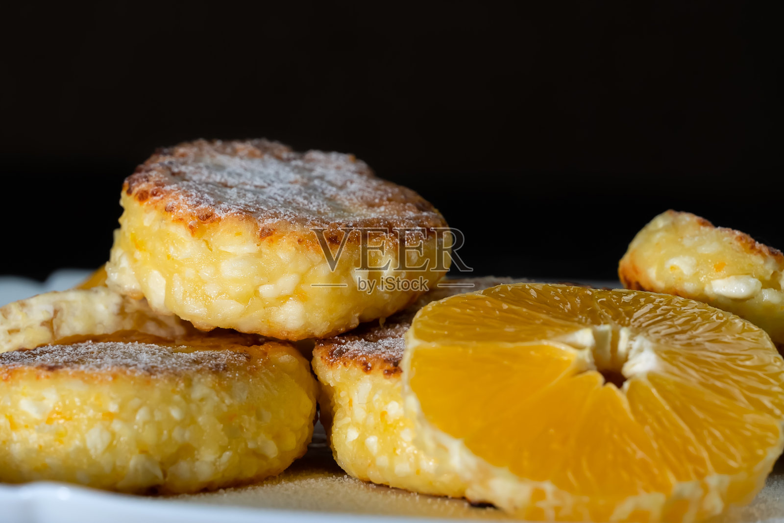 甜白软干酪煎饼与橙色片在一个白色盘子近距离对着黑色的墙与复制空间。照片摄影图片