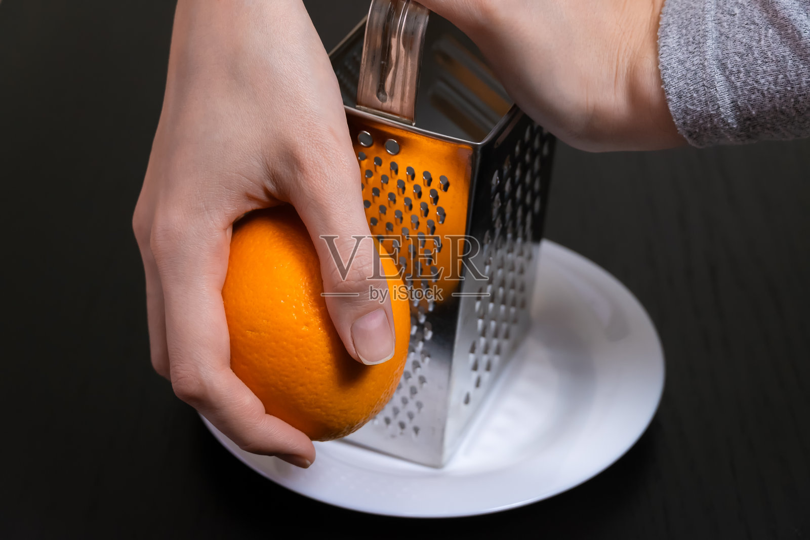 女厨师在一个白色盘子上用刨丝器磨碎橙子皮照片摄影图片